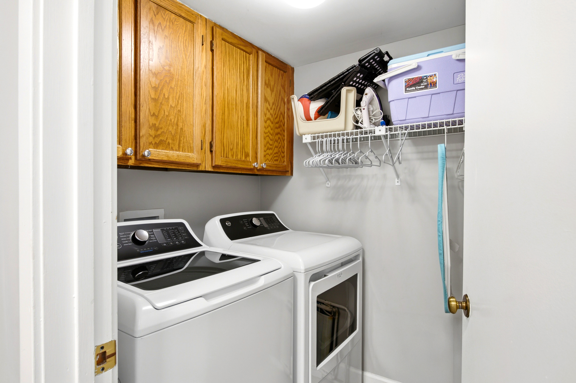 Organized efficiency meets homey warmth in this dedicated laundry nook. Honey-toned oak cabinetry provides ample storage above modern appliances, creating a tidy and practical space for refreshing your wardrobe during a long stay.