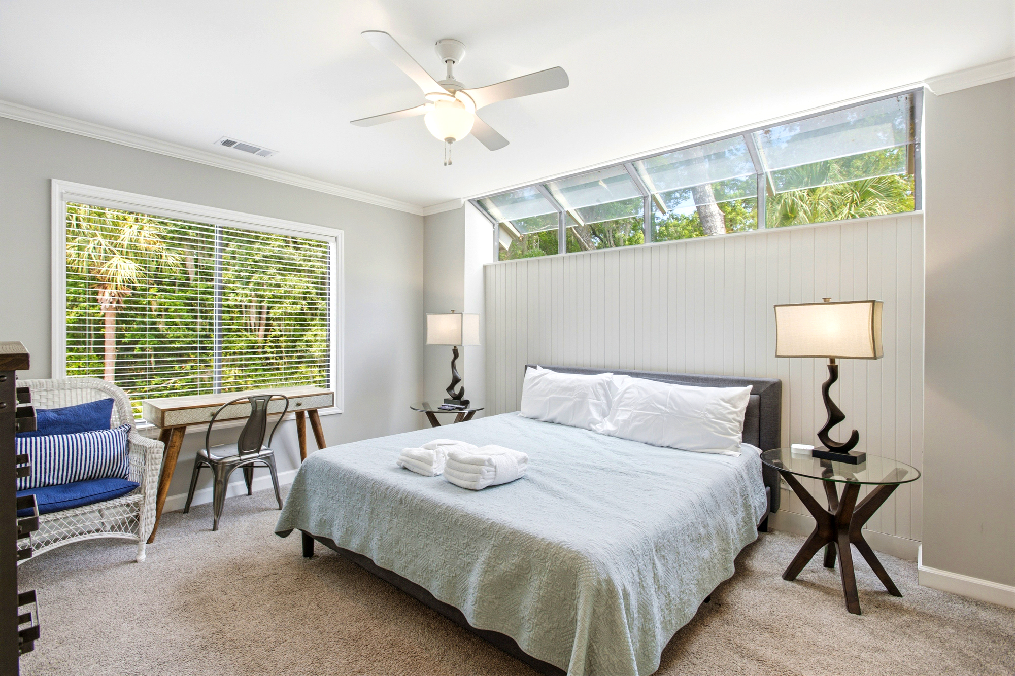 Angled skylights pour a gentle afternoon glow over the plush king bed and crisp shiplap walls. Lush greenery peeks through the windows, creating a peaceful garden backdrop for your morning coffee at the vintage-style desk.