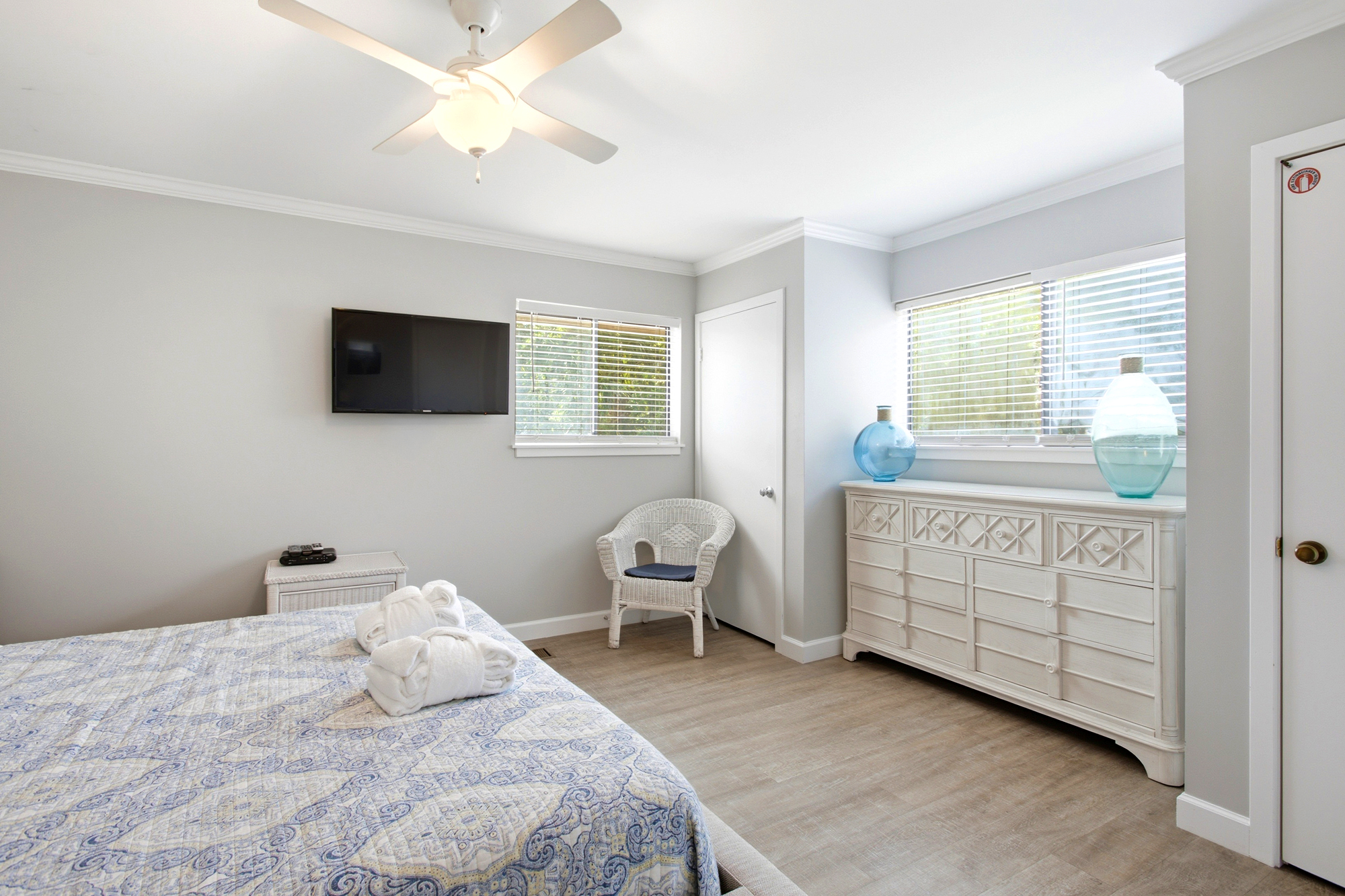 Coastal textures meet airy design in this serene bedroom, where wicker accents and sea-glass tones create a calming escape. Bright walls catch the gentle daylight, highlighting the patterned quilt and spacious dresser for a restful stay.