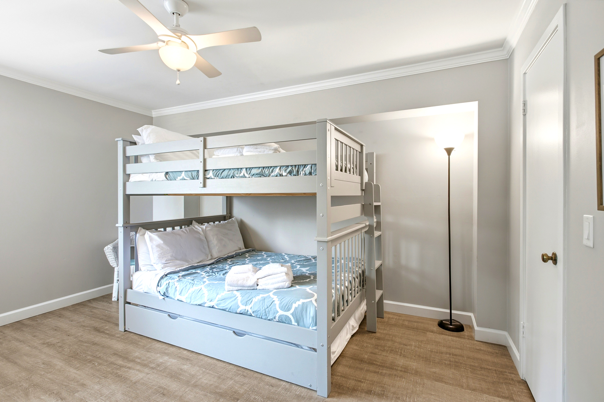 Dove-gray bunk beds offer a cozy corner for rest, paired with geometric linens and smooth wood-style flooring. A warm floor lamp glows against the neutral walls, creating a calm and quiet space for a peaceful night.