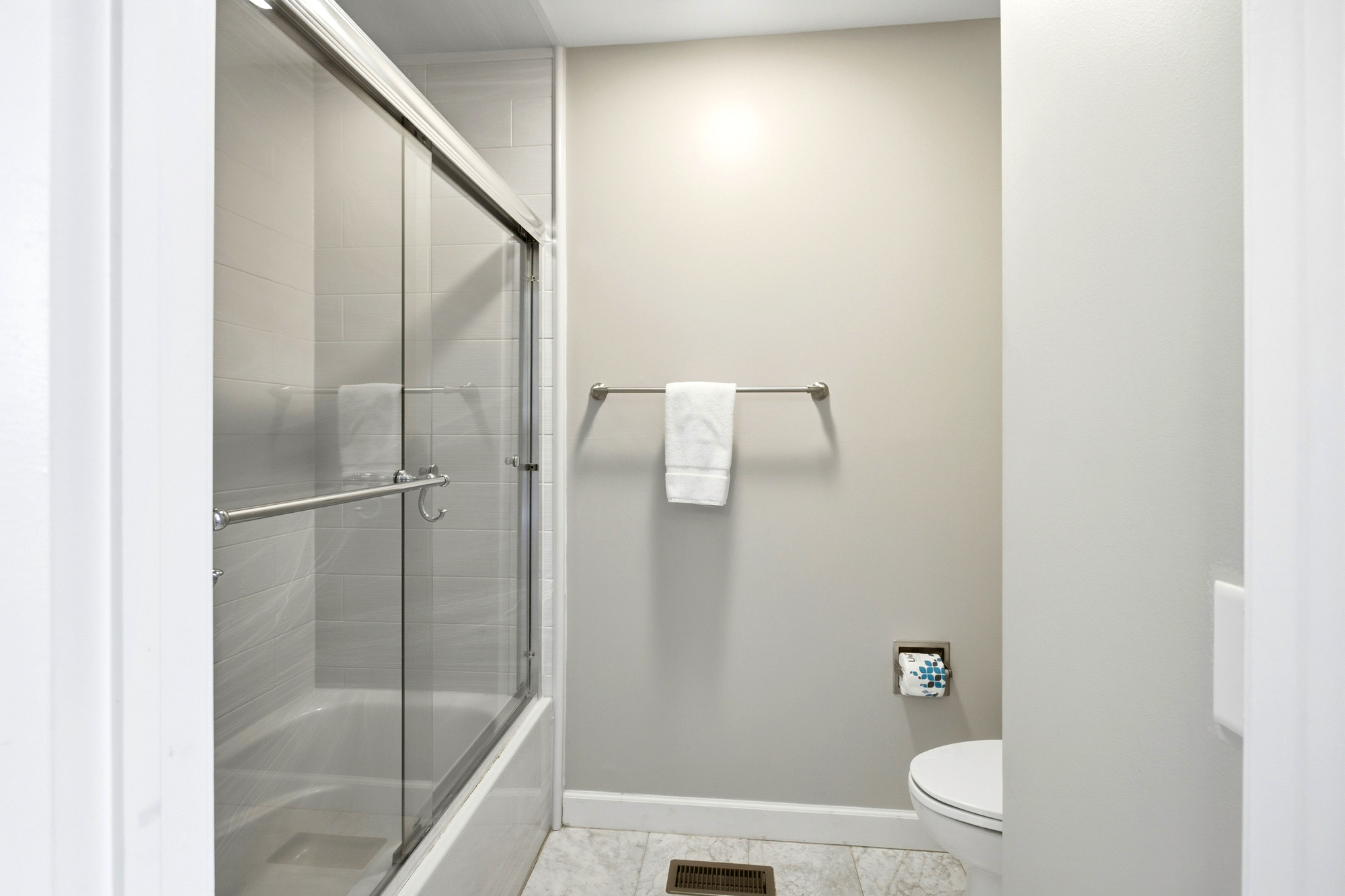 Glass doors and clean white tiles create a bright, airy feel in this contemporary bathroom. A soothing neutral palette and overhead glow offer a calm space to prepare for your day.