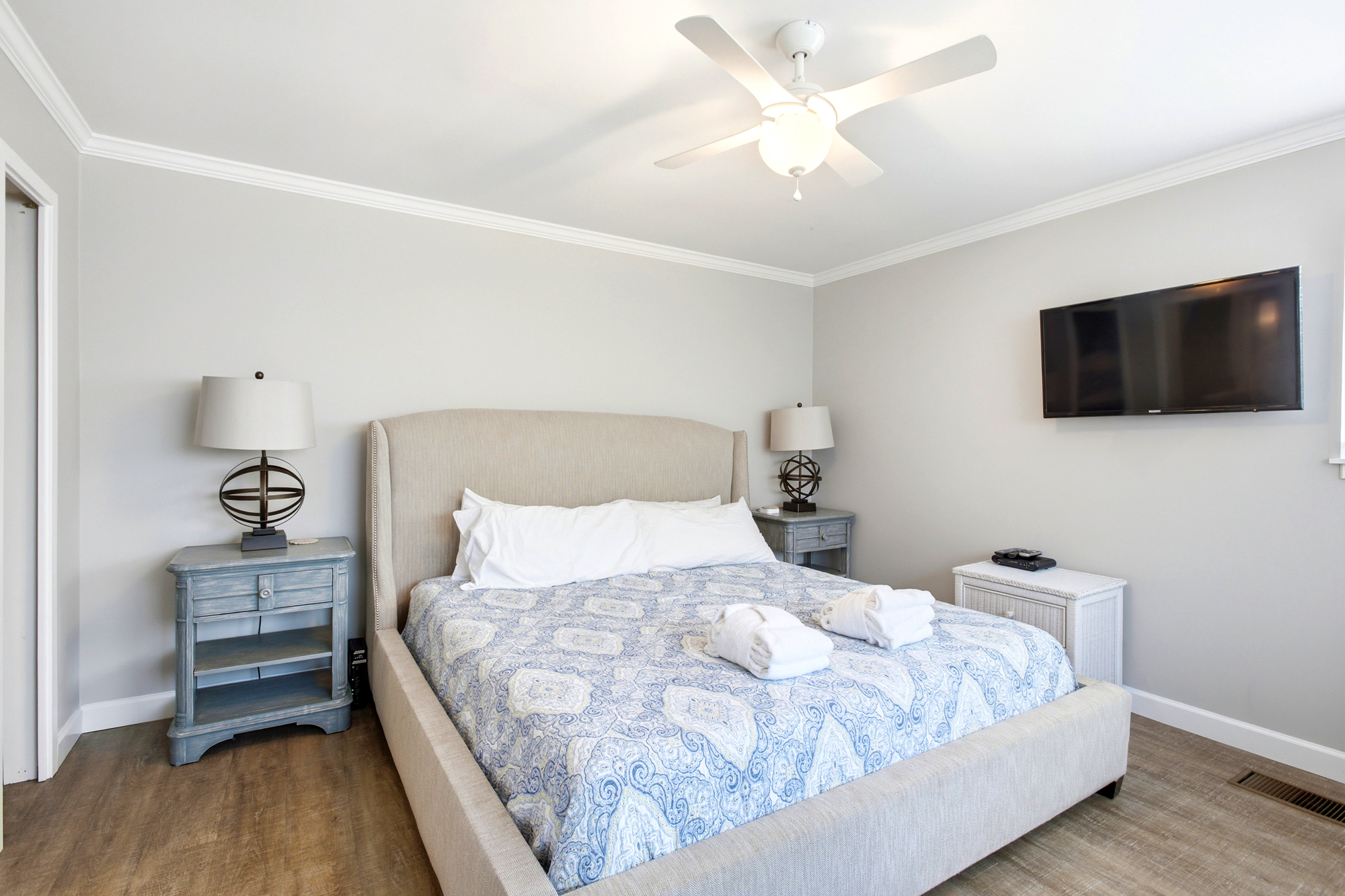 Blue patterned linens and plush robes promise a restful stay in this airy bedroom. Distressed wood nightstands and a padded headboard create a calm, tactile space for quiet evenings.