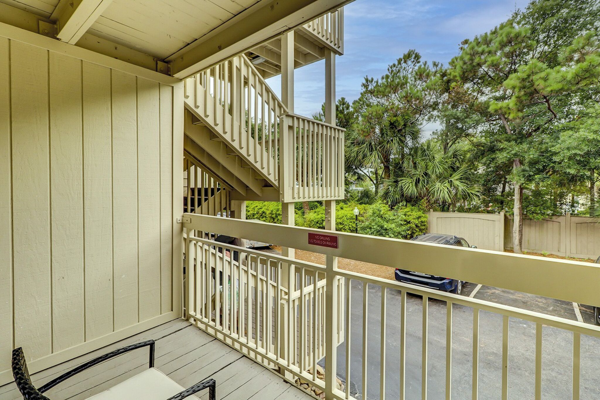 Timber railings and soft cream siding frame this breezy outdoor nook, where shadows dance across the gray wood decking. Lush palms peek through the balconies, inviting you to pause and breathe in the fresh garden air.