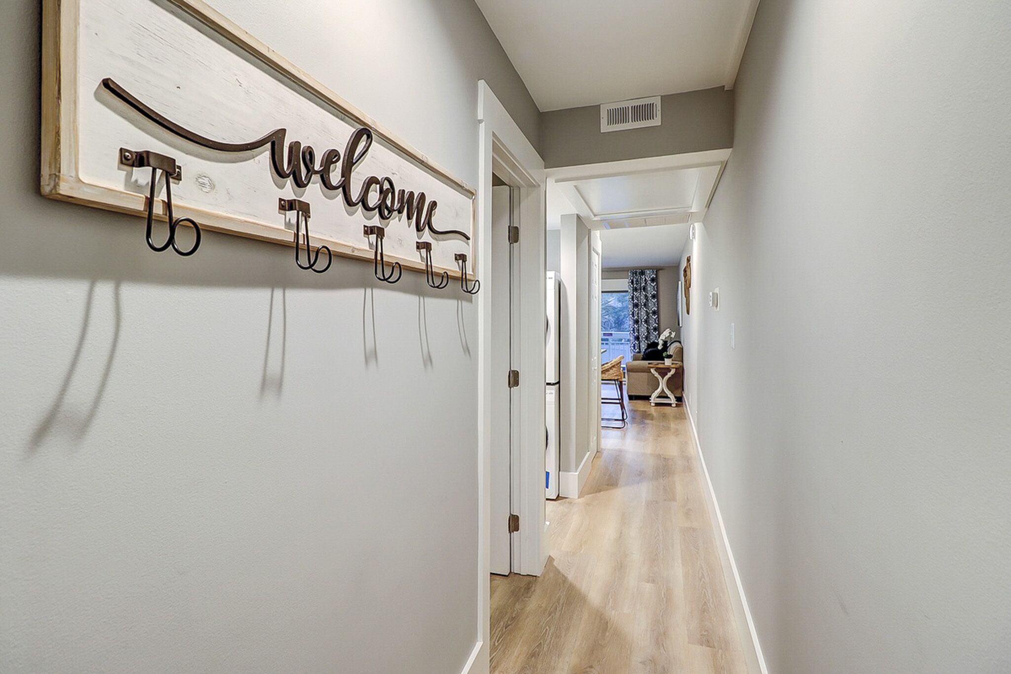 Weathered wood and wrought iron accents line the entryway, leading your eye down a sunlit corridor of pale oak flooring. Soft grey walls and clean lines create a calm, airy transition into the heart of the home.
