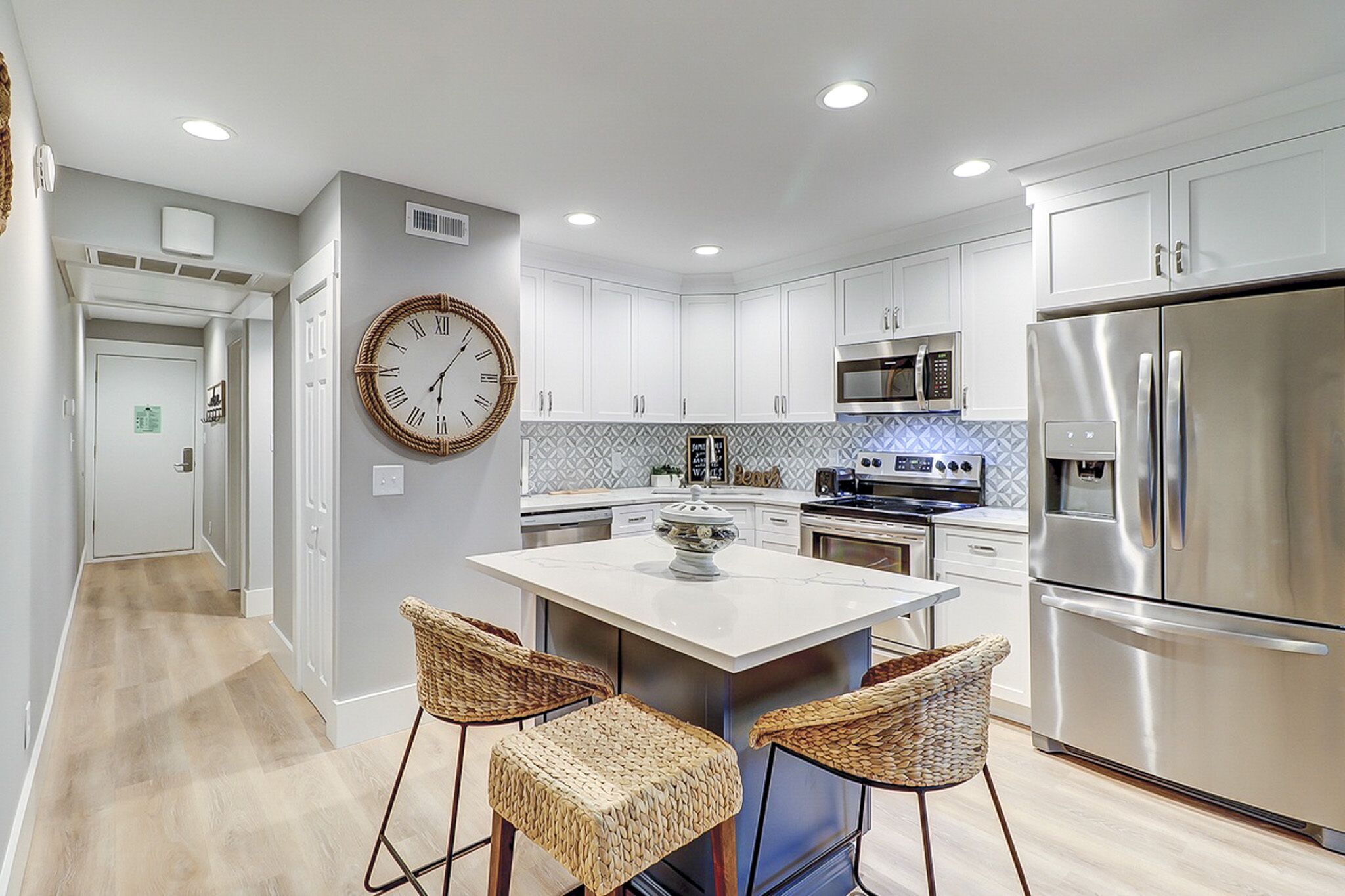 Seagrass barstools add organic texture to this bright kitchen, where patterned tiles and sleek quartz surfaces shimmer under soft recessed lighting. It is a modern, airy space perfectly suited for slow mornings and shared meals.