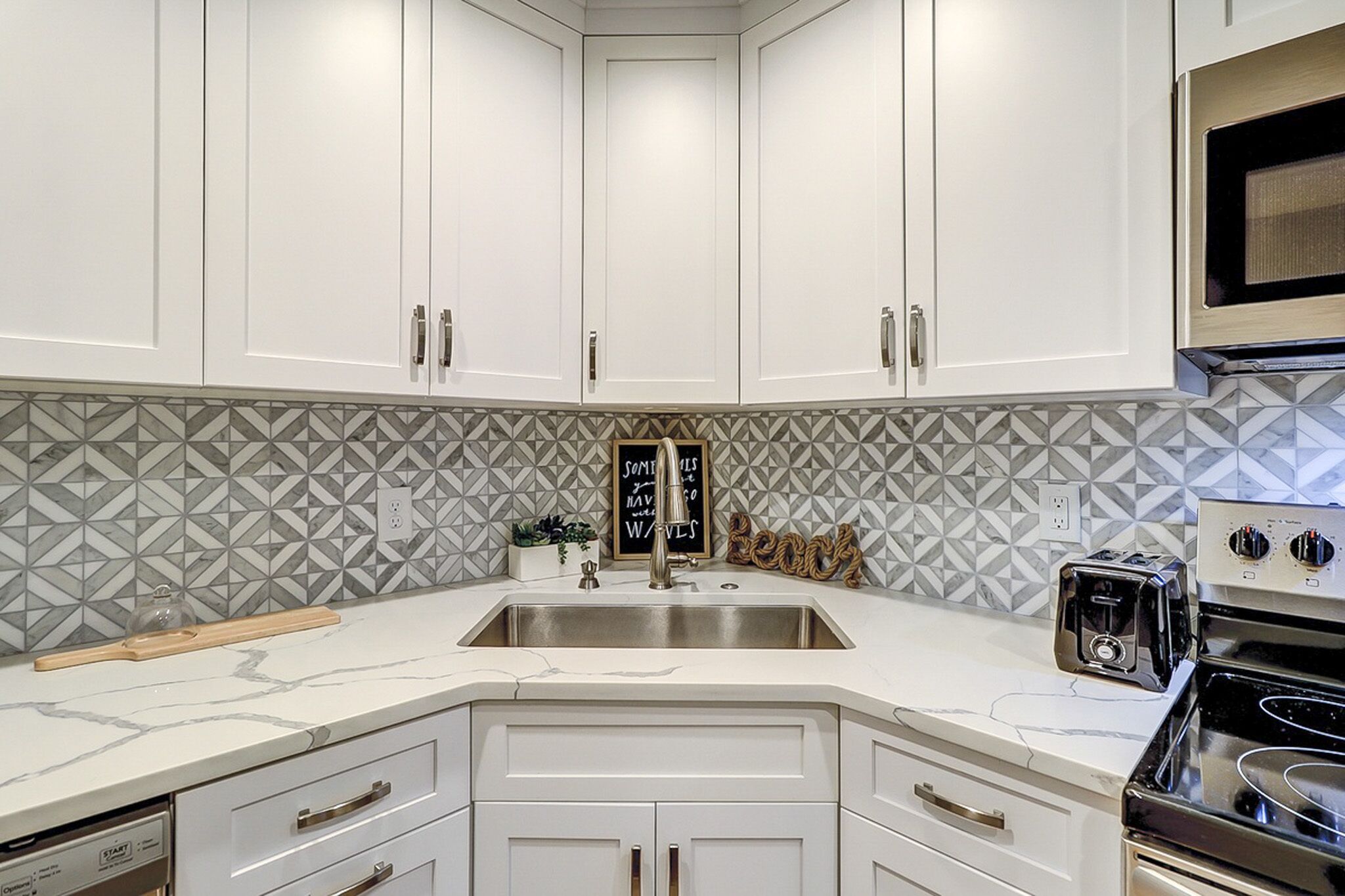 Geometric marble tiles create a striking backdrop for this bright chef's corner. Smooth stone countertops and sleek white cabinetry offer a clean, airy space to prep morning coffee or a quiet dinner at home.