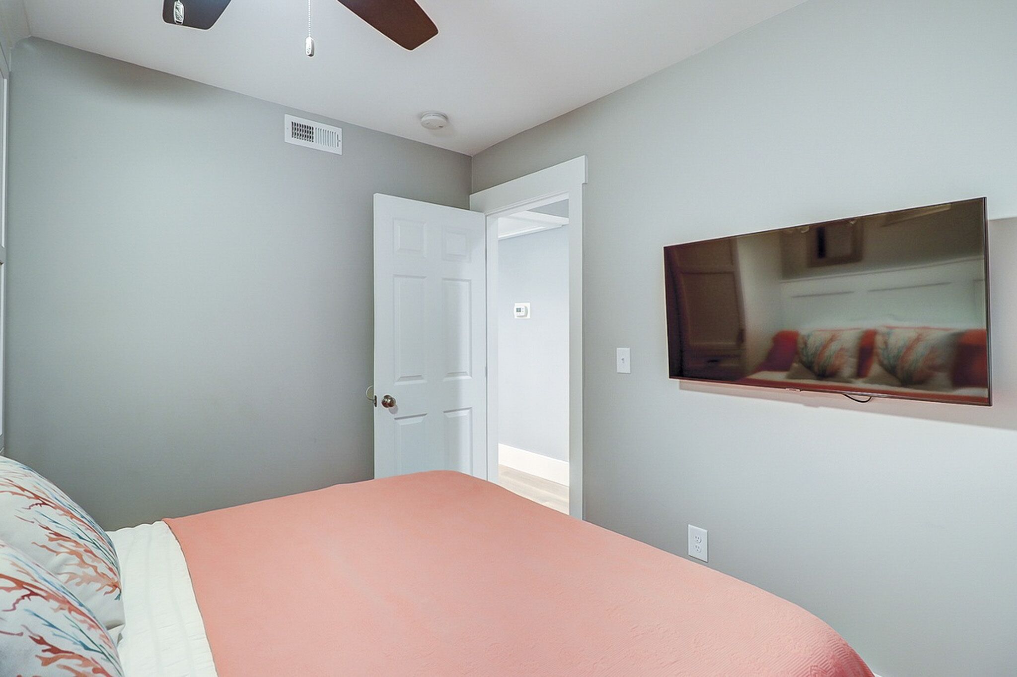 Peach hues and soft grey walls create a calm, quiet sanctuary for a restful night. A wall mounted screen offers easy entertainment from the comfort of the plush bed, while the airy layout feels open and bright.