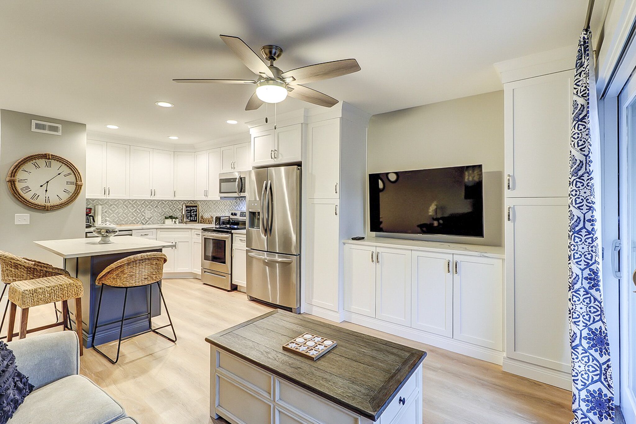 Crisp white cabinetry and cool navy accents create a bright, airy hub for your coastal mornings. Natural textures like the wicker seating and weathered wood table add a grounded, tactile comfort to this open, sun-washed living area.