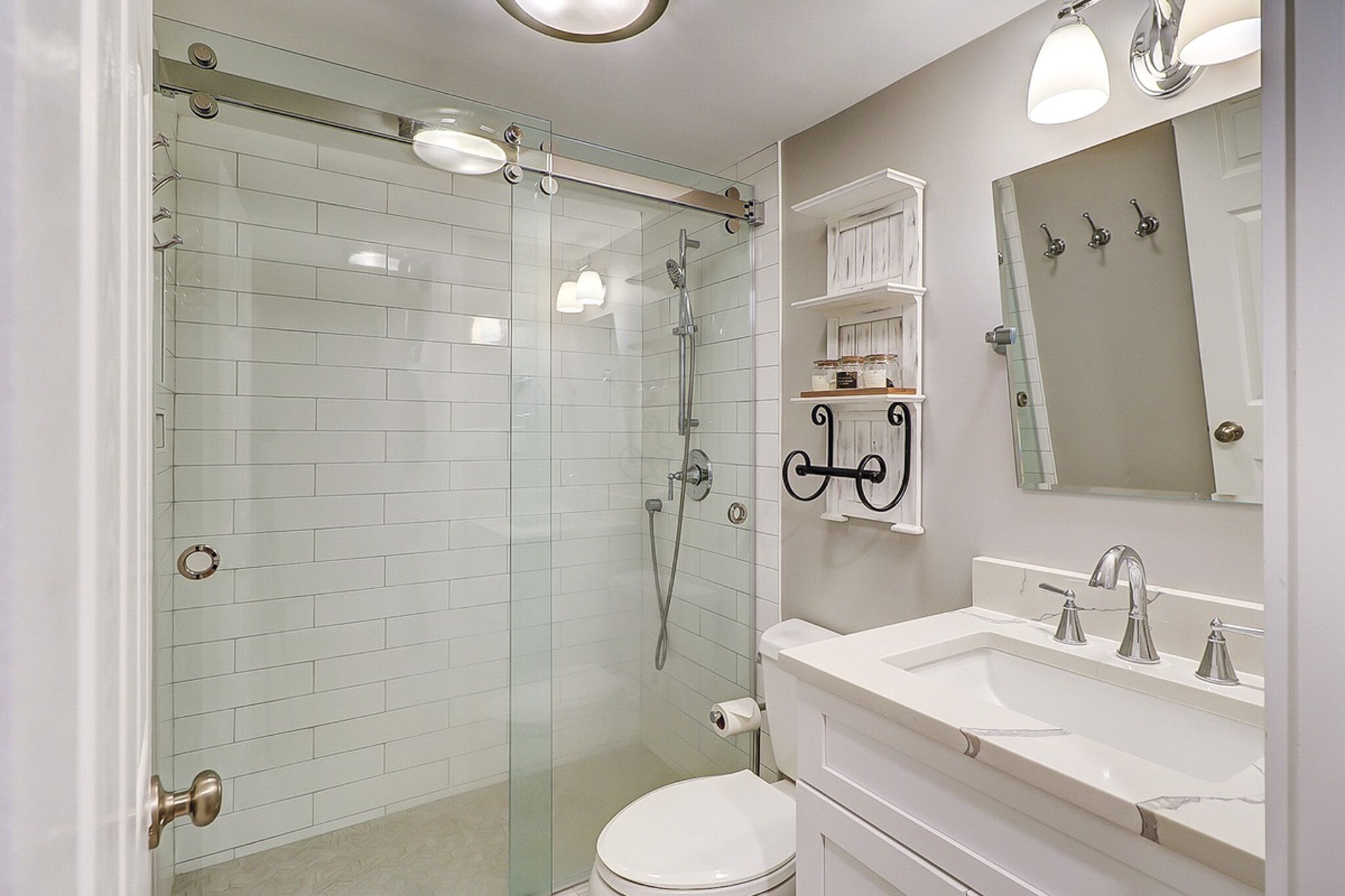 White subway tiles and sleek glass doors create a bright, airy atmosphere in this modern bathroom. Soft overhead lighting reflects off the marble vanity and chrome fixtures, offering a clean and restorative space to start your morning.