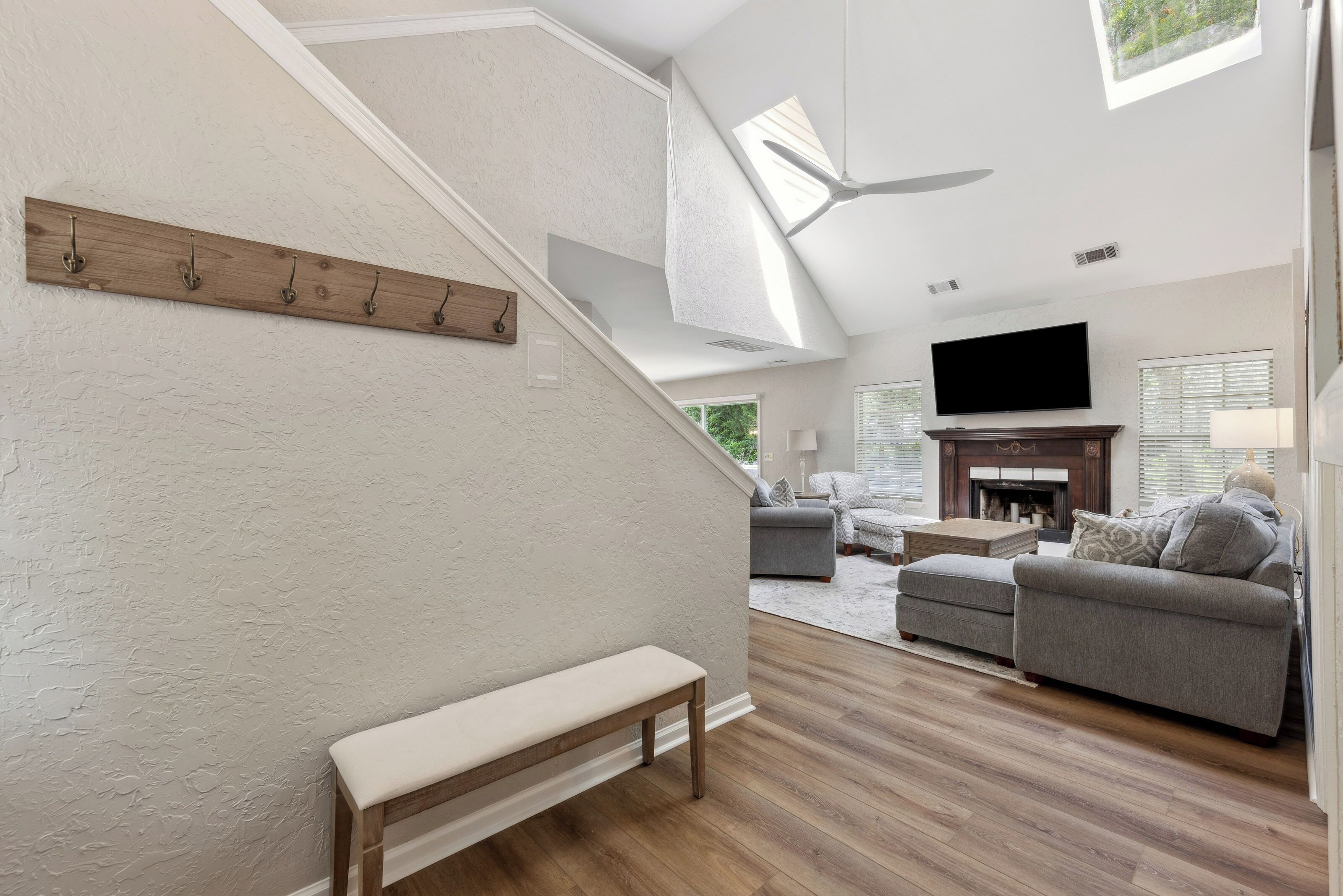 Natural light pours through high skylights to illuminate the textured walls and rich wood floors of this airy living space. A handsome fireplace and plush seating create a cozy anchor for slow mornings or quiet evenings by the hearth.