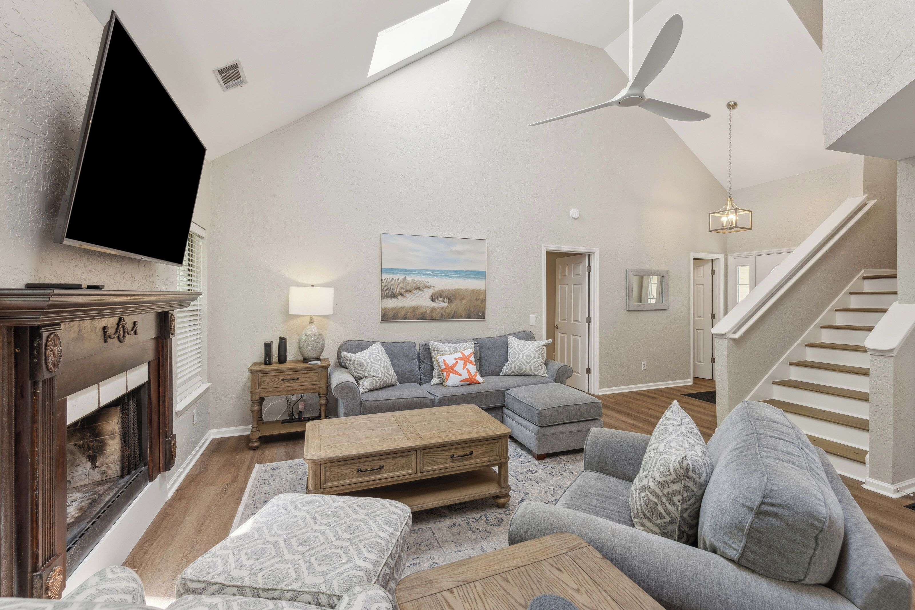 Angled ceilings and a crisp skylight create an airy volume over this serene lounge. Soft grey fabrics and carved wood accents anchor the room, while the glow from the hearth makes it a perfect spot for quiet evenings together.