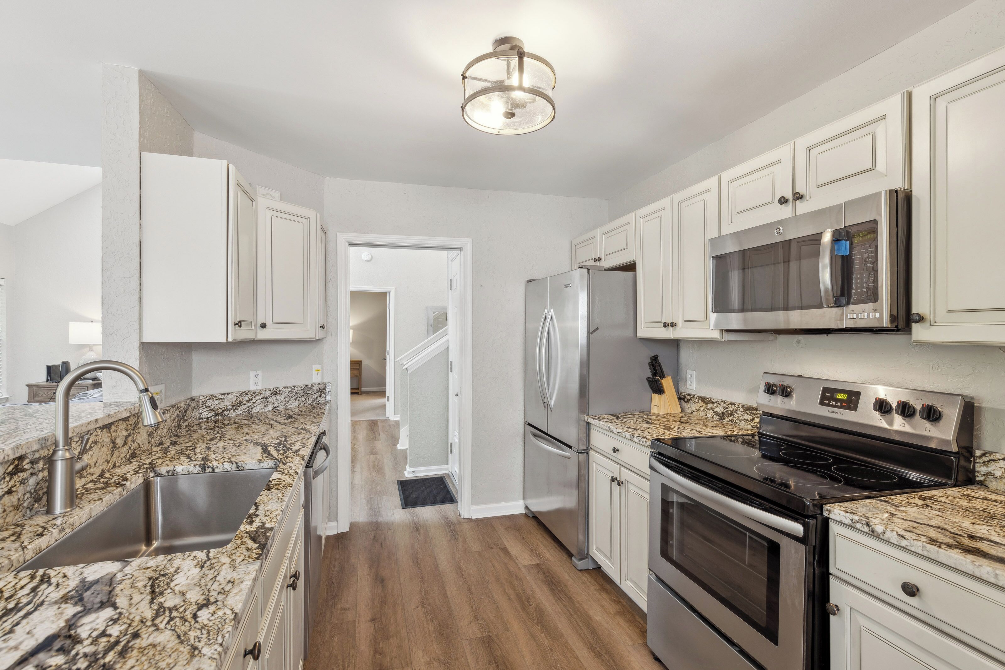 Intricate patterns of earth-toned counters meet sleek stainless steel in this chef-ready kitchen. Soft overhead light gleams across the white cabinetry and rich wood floors, creating a crisp, inviting space for morning coffee or evening meals.