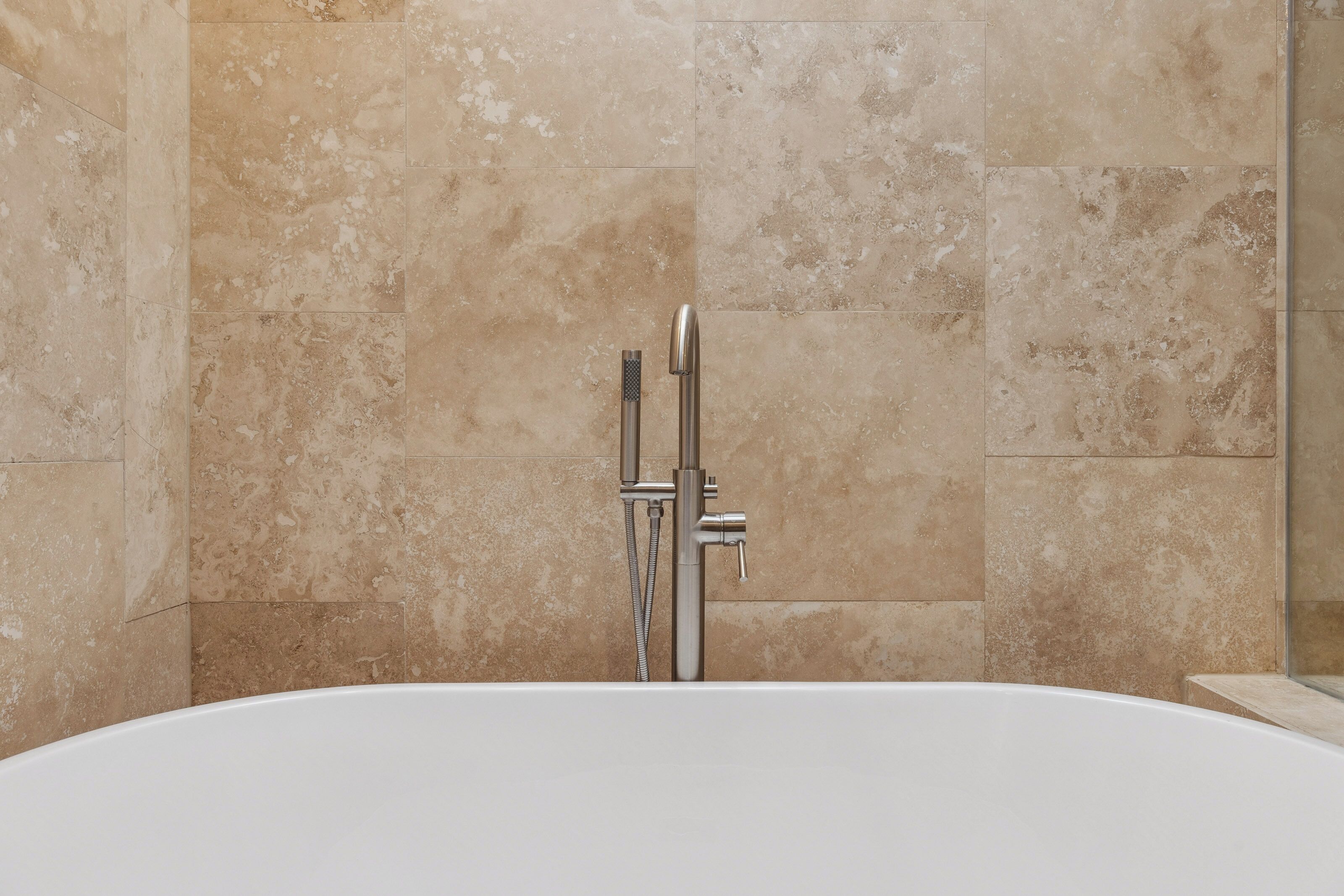 Brushed nickel fixtures stand in elegant contrast against textured sand colored tiles. This deep soaking tub offers a serene corner for quiet reflection and a spa like rinse after a long day of travel.