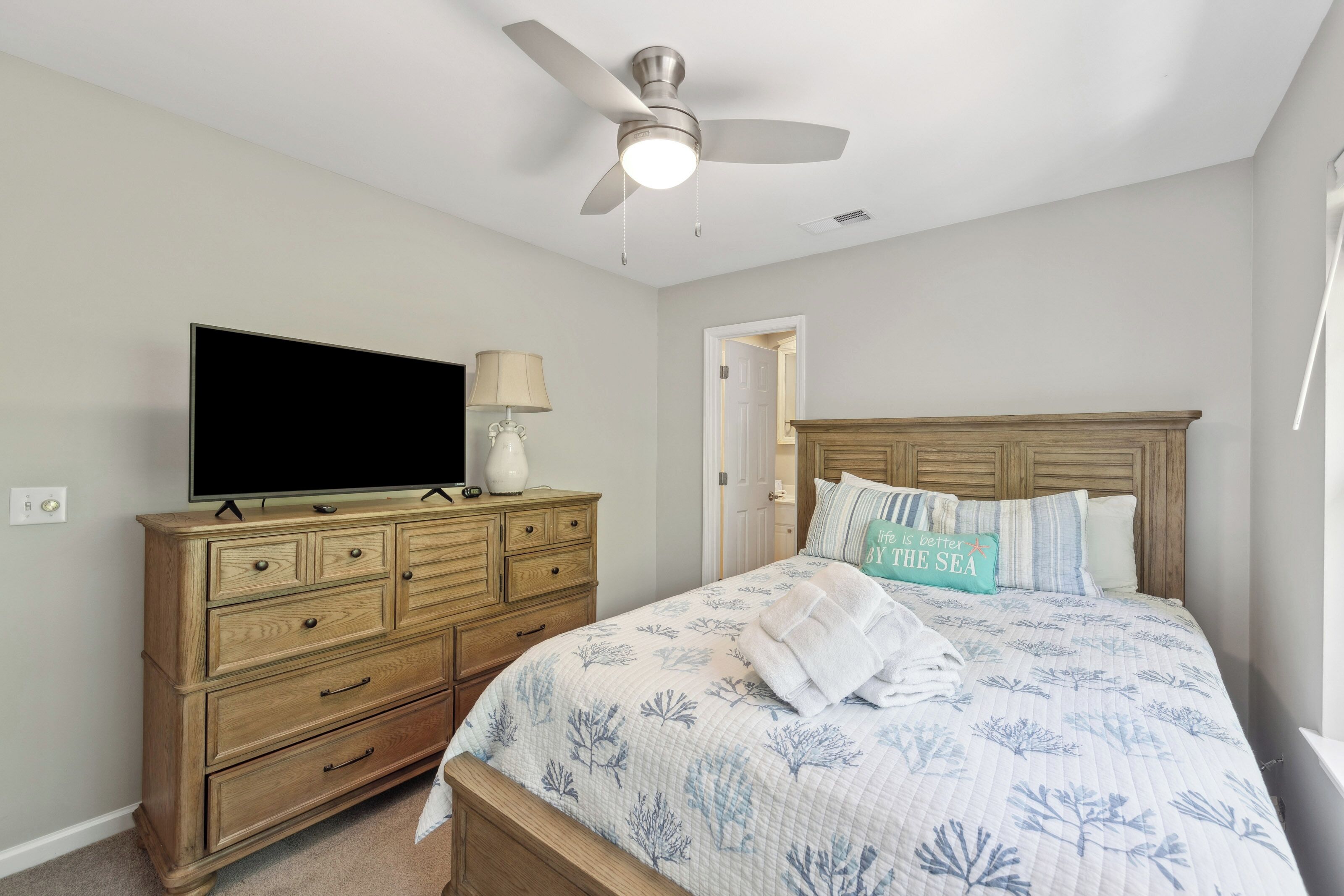 Driftwood tones and coastal patterns create a soothing sanctuary for your stay. Crisp linens and a gentle ceiling breeze invite you to linger over movies or simply rest in the quiet, sunlit glow of this peaceful bedroom.