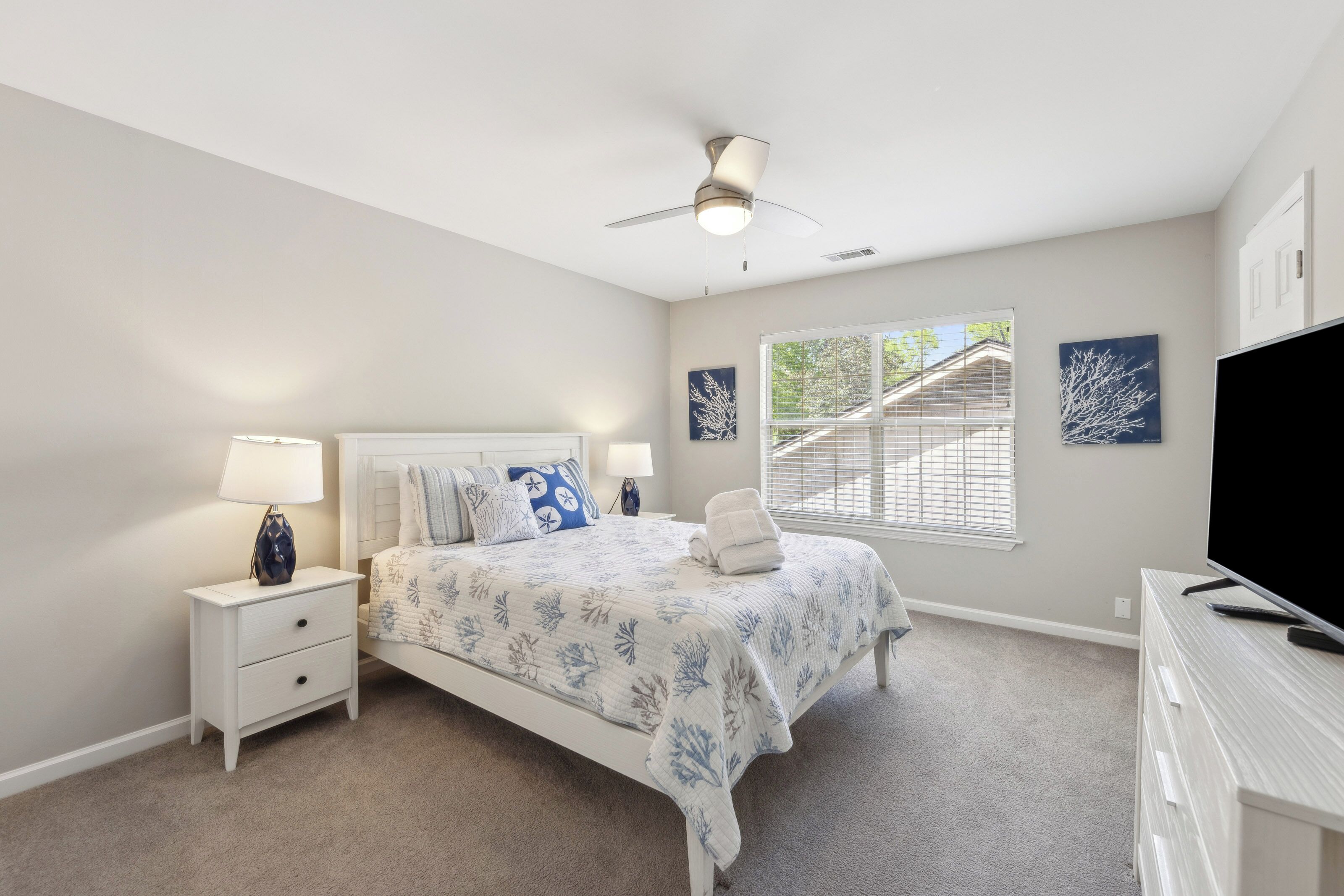 Soft coastal tones and coral patterns create a serene escape, where gentle morning light pours through the window. Crisp white linens and plush carpets offer a quiet, airy space to rest and recharge.