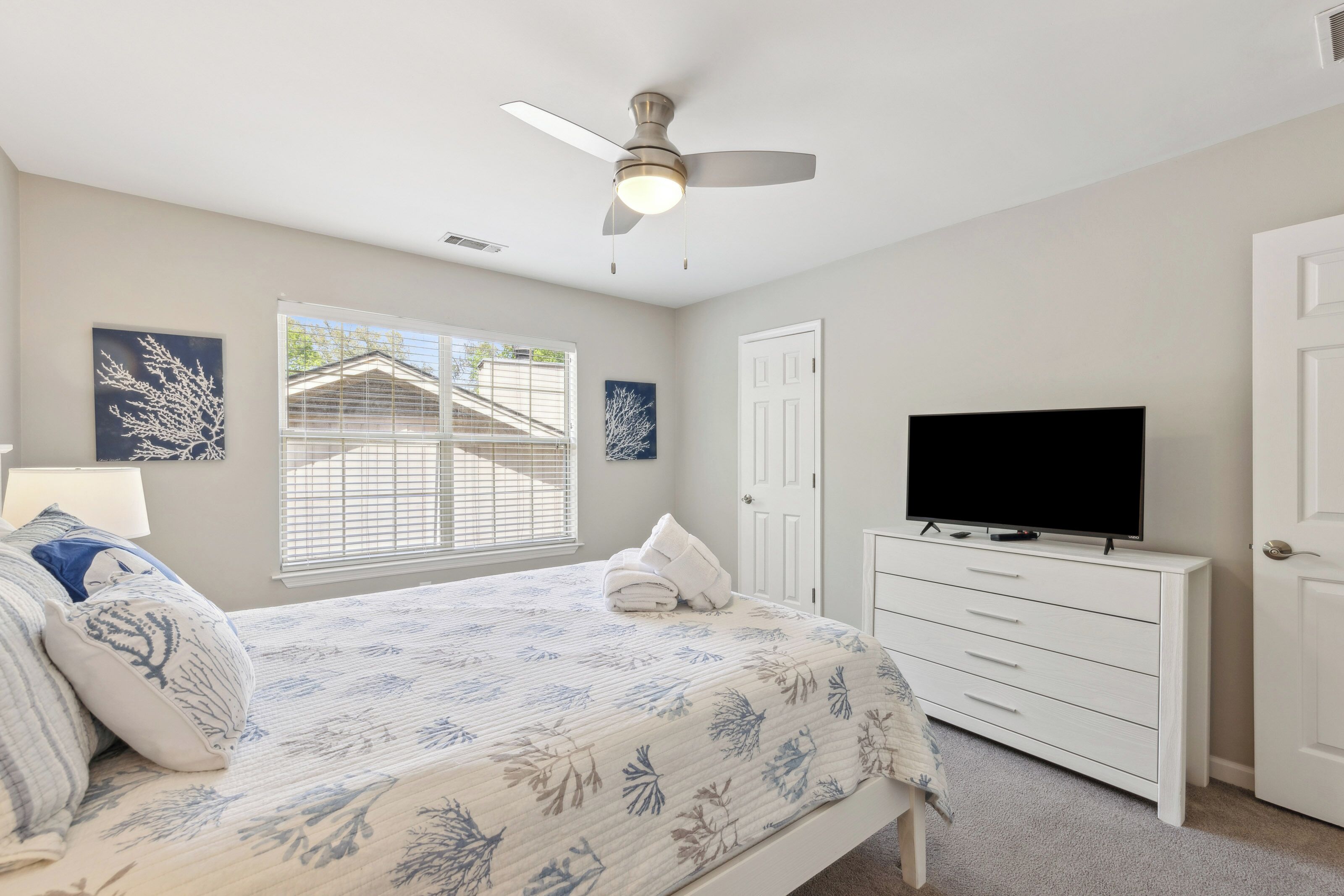 Cool coastal patterns and crisp white linens create a serene sanctuary for your stay. Gentle afternoon rays filter through the blinds to illuminate the brushed nickel accents and calming blue decor, making this a perfect spot for quiet mornings.