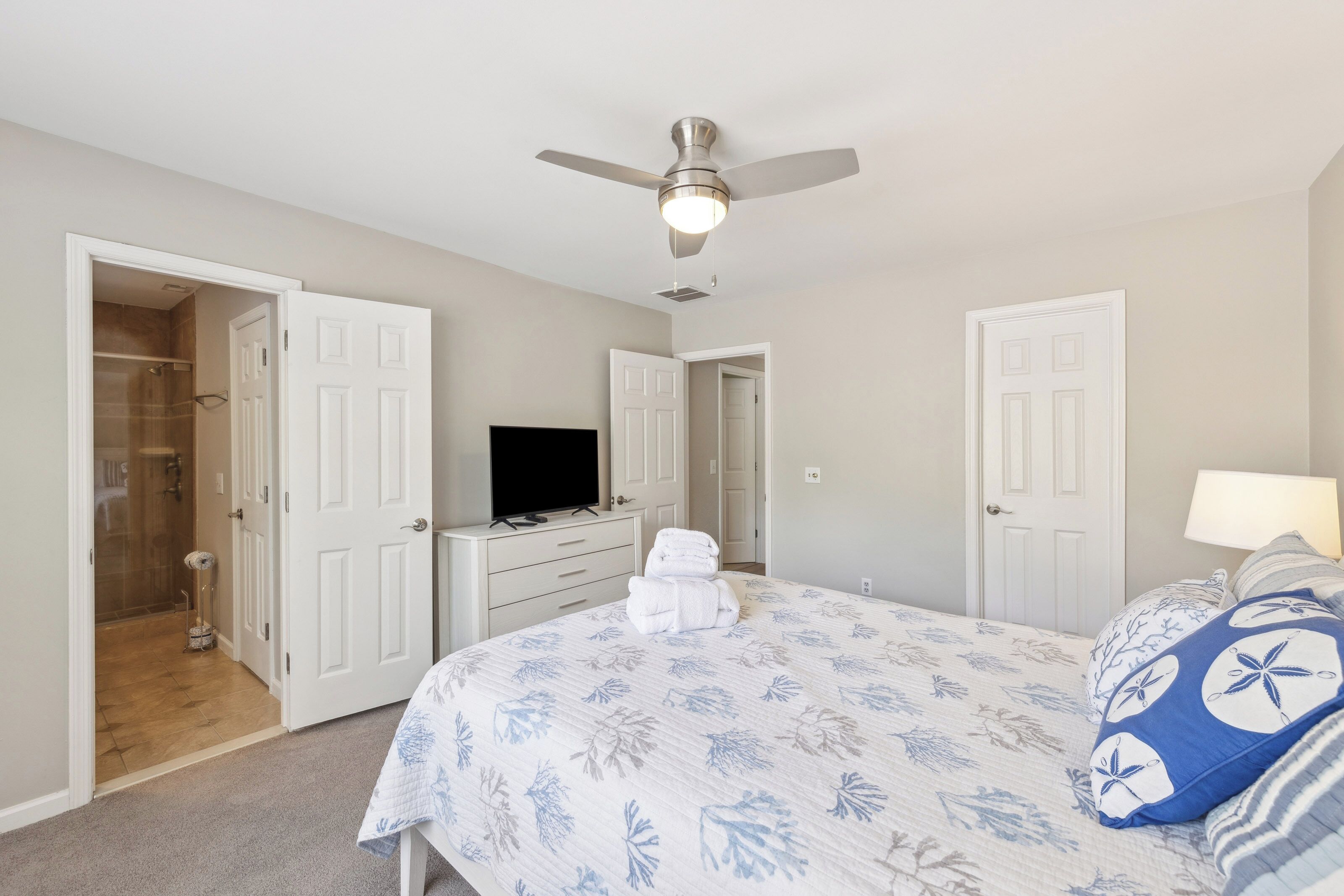 Coastal blues and crisp white linens create a serene sanctuary, anchored by a plush bed and private ensuite bath. Modern finishes and a gentle overhead breeze ensure a restful night after a day at the beach.
