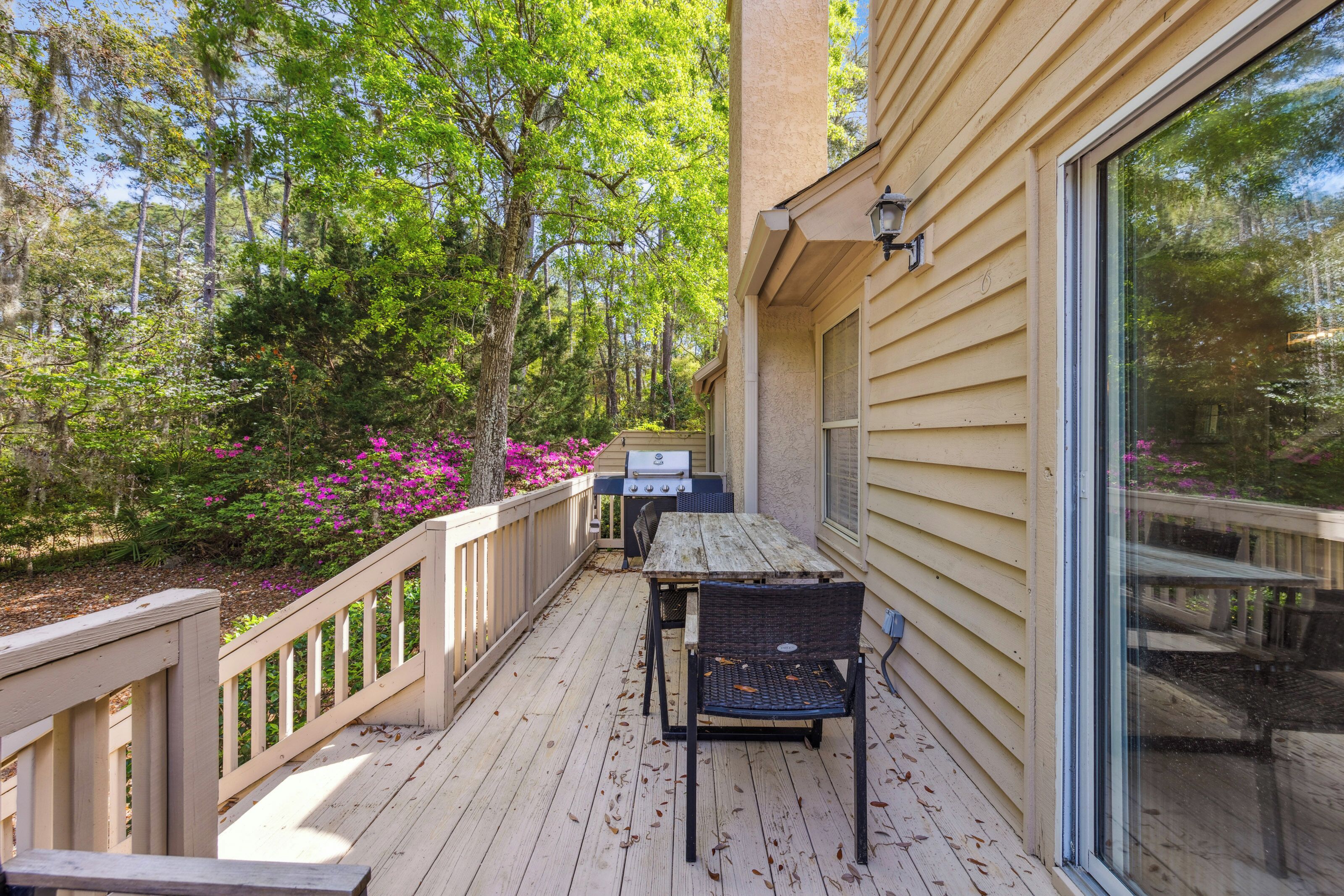 Timber planks stretch toward a bright forest canopy, creating a quiet spot for alfresco dining. Vibrant pink blooms and a sun-drenched grill area offer a peaceful backdrop for slow afternoons spent in the fresh air.