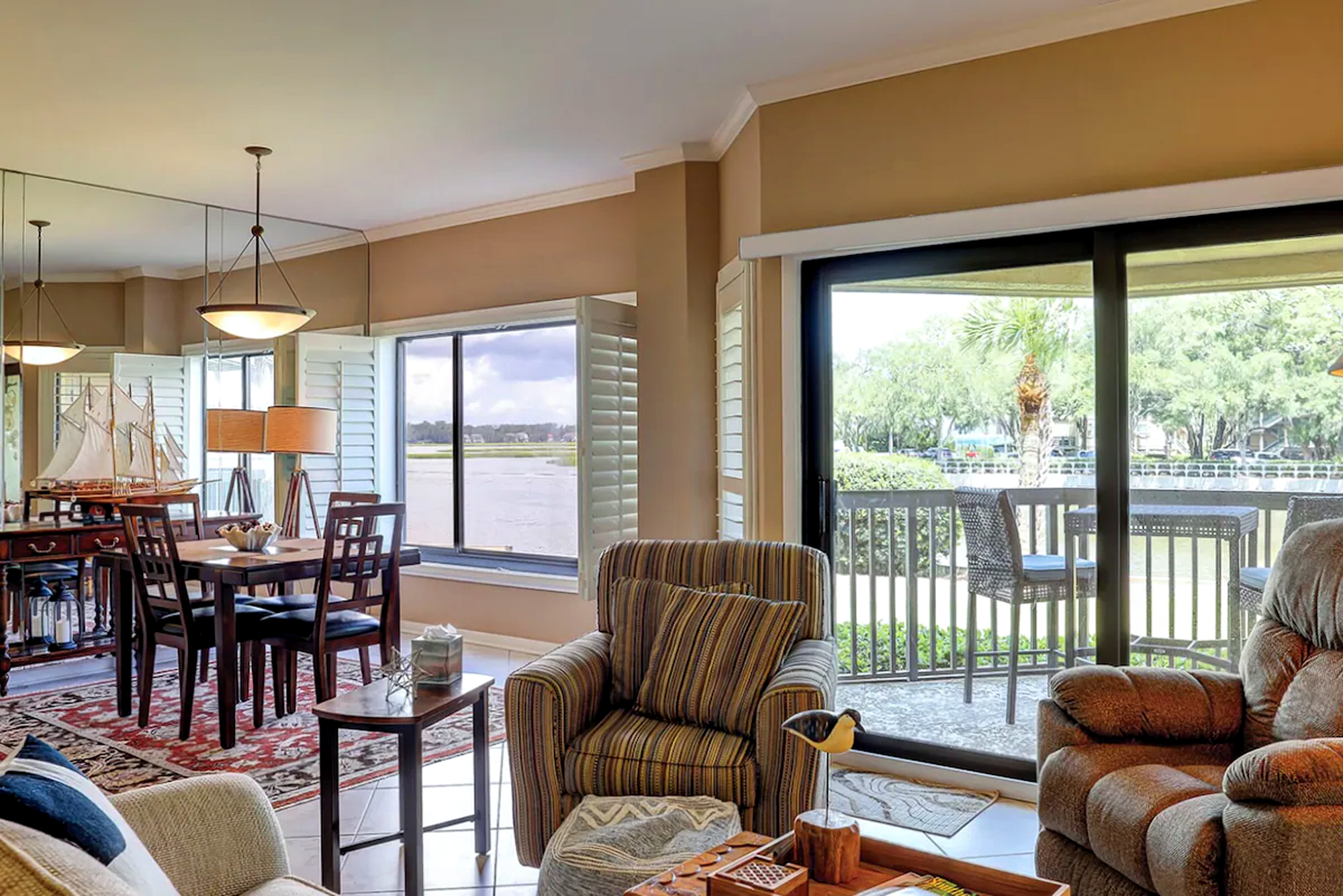 Plush armchairs and warm wood finishes create a cozy corner perfect for watching the tides. Floor to ceiling glass doors pull the coastal scenery inside, filling the room with a soft afternoon glow and views of the quiet water.