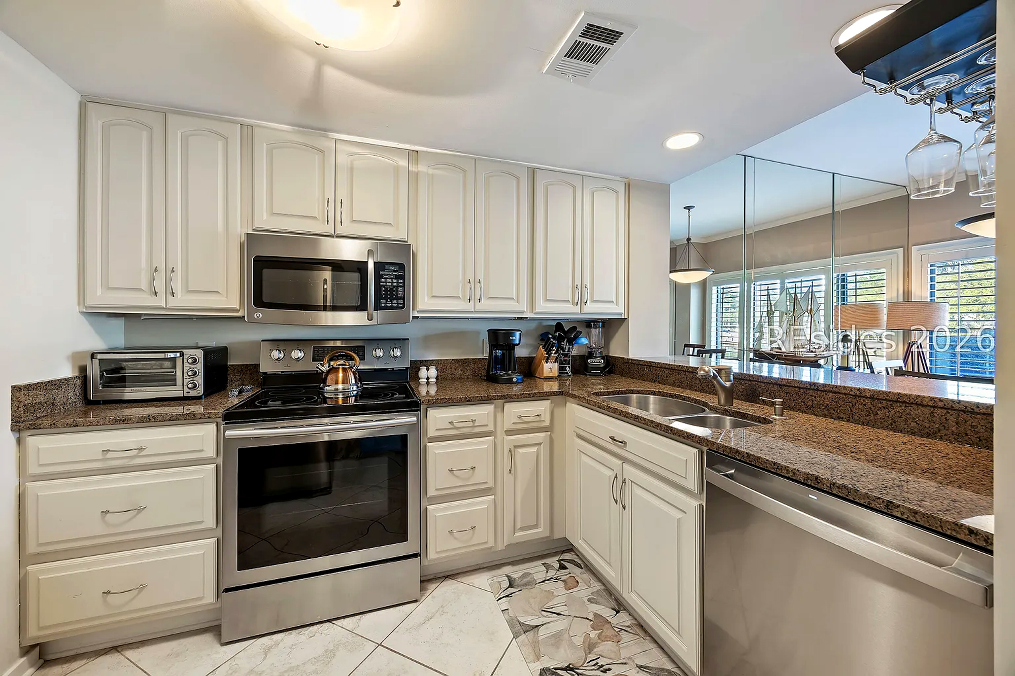 Polished granite countertops and stainless appliances anchor this bright kitchen, where morning light reflects off clean white cabinetry. A mirrored backsplash opens the room, creating an airy atmosphere for brewing coffee or preparing a meal.