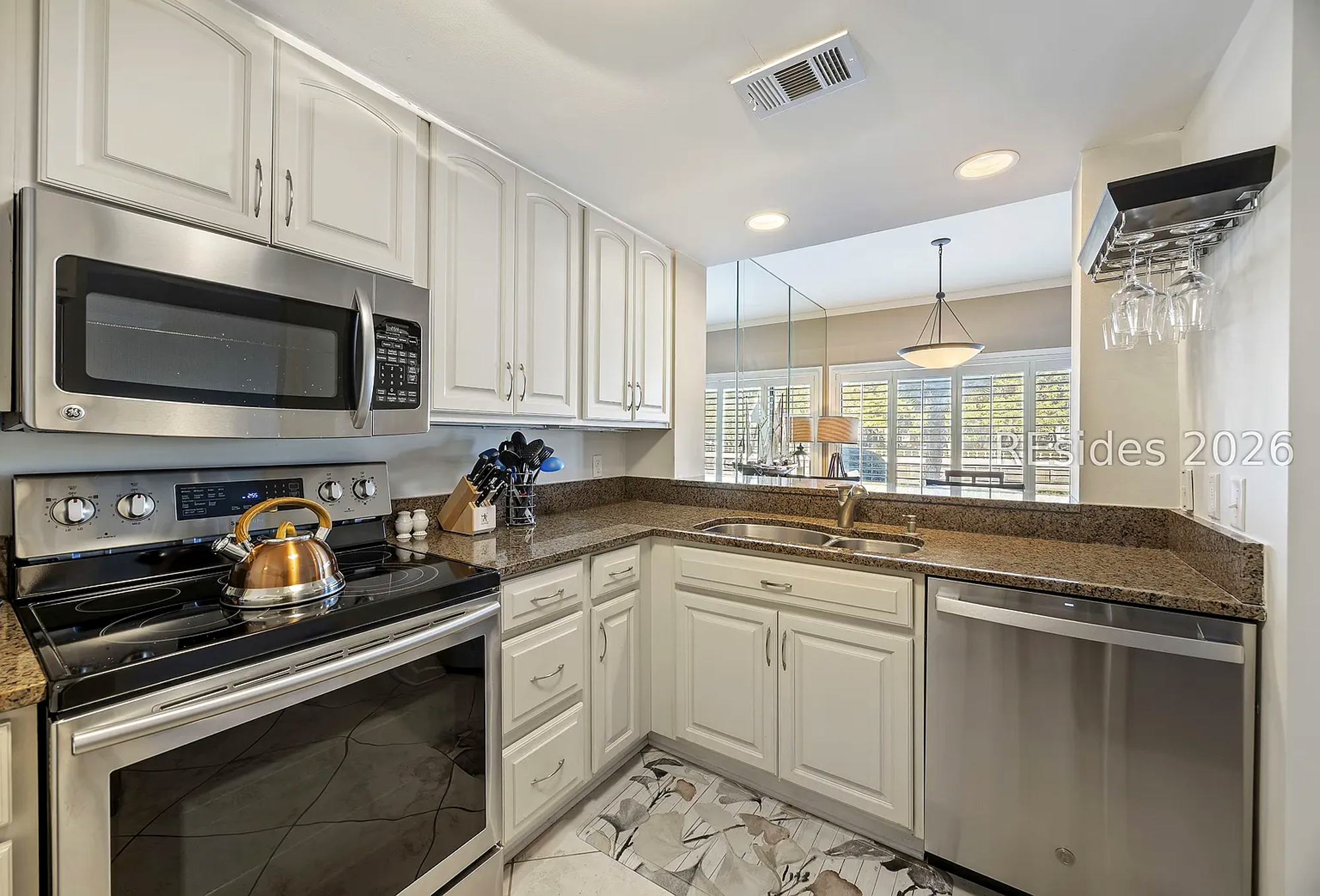 Granite counters and stainless steel appliances create a sleek, modern kitchen space. Bright white cabinetry reflects the soft glow from the dining area, offering a clean and airy corner to prepare your morning coffee.