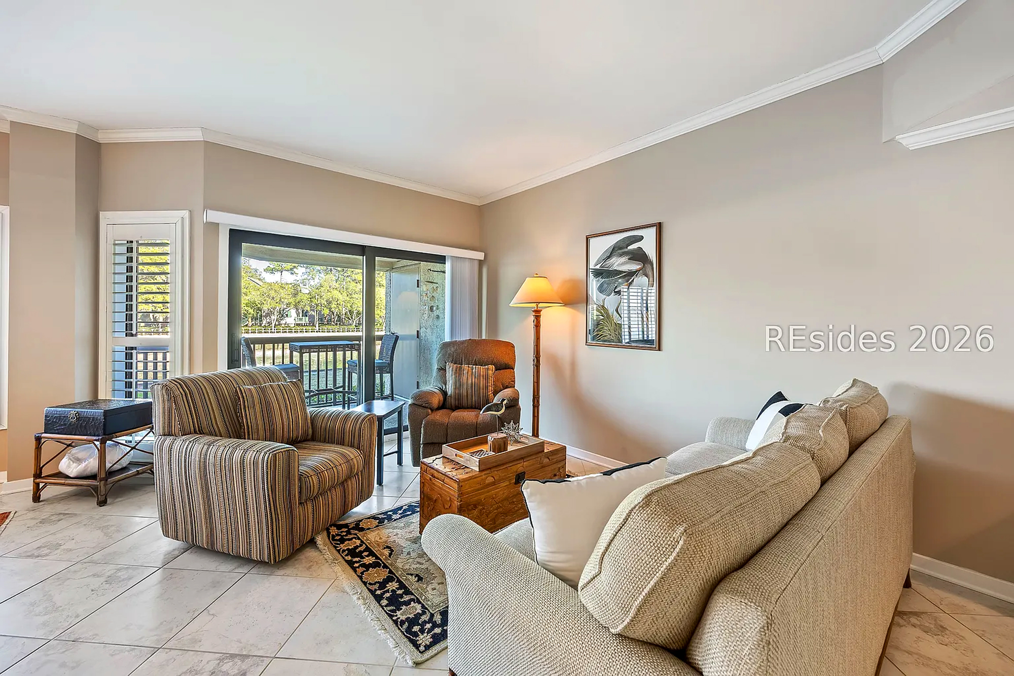 Earth tones and woven fabrics create a grounded, cozy atmosphere in this airy living space. Natural radiance pours through the glass doors, illuminating the tiled floors and handcrafted wood accents for a bright, peaceful afternoon indoors.