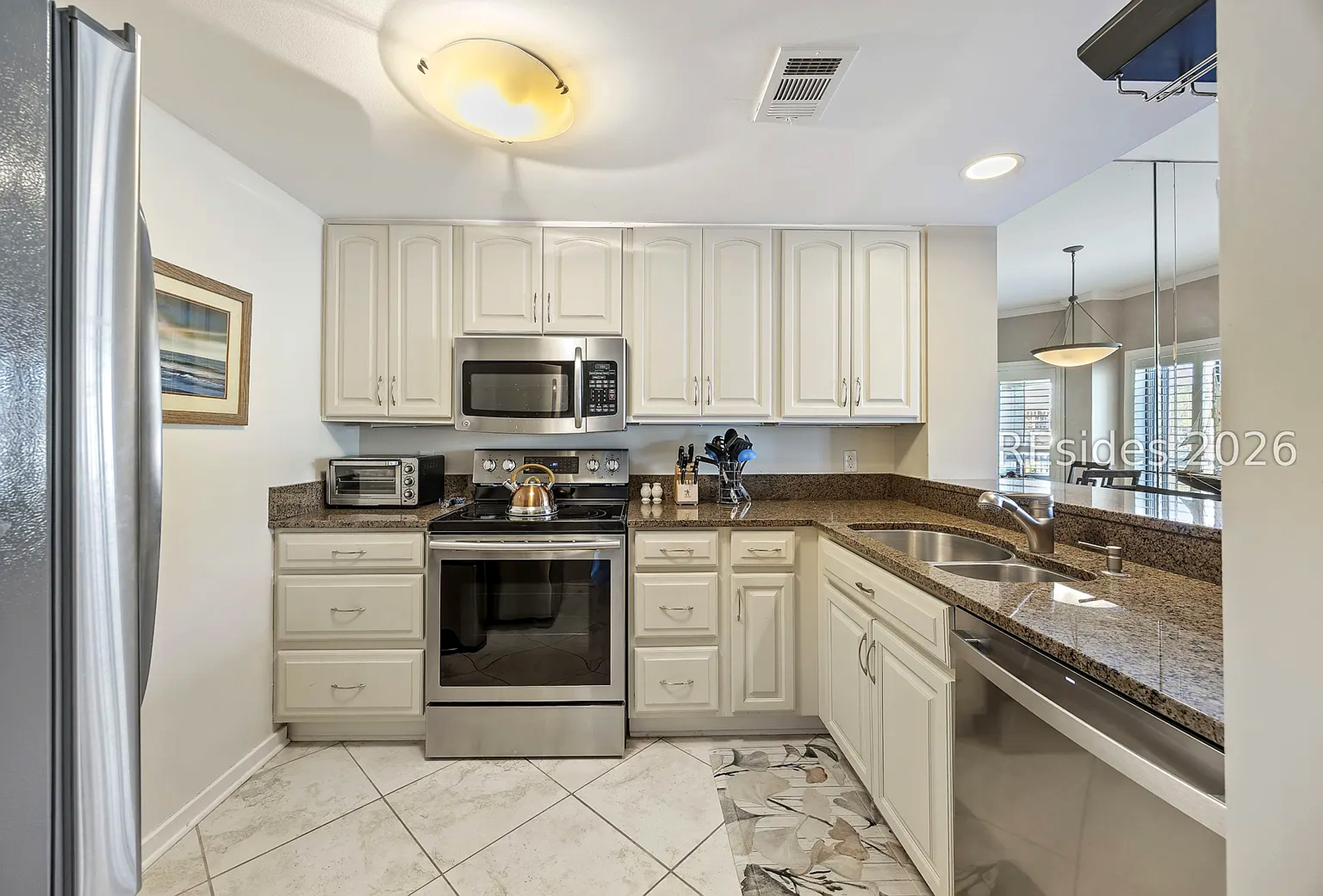 Ivory cabinetry and sleek stainless appliances anchor this bright kitchen, where a soft interior glow reflects off the dark countertops. Tiled floors and ample counter space create a clean, modern setting for preparing your favorite vacation meals.