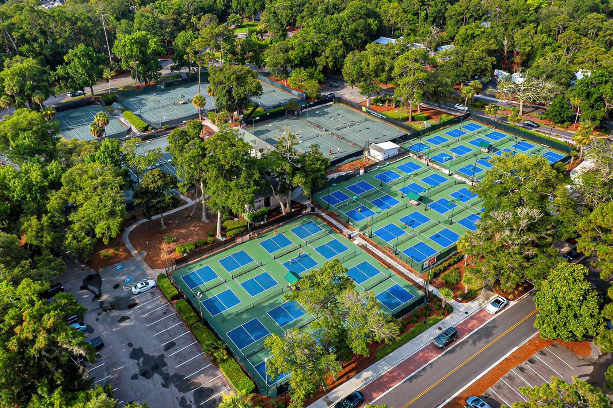 Vibrant blue courts pop against a canopy of ancient oaks and leafy pines. This sprawling recreation area offers a professional setting for an afternoon match under the bright coastal sky.