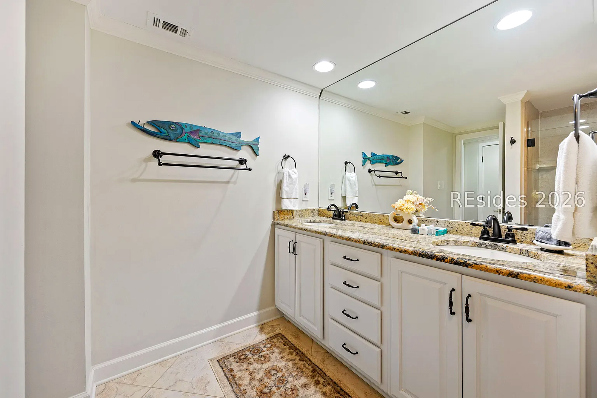 Coastal charm meets modern convenience in this airy bathroom, featuring playful wood art and a spacious double vanity. Natural tones and bright fixtures create a refreshing space to prepare for your day by the water.
