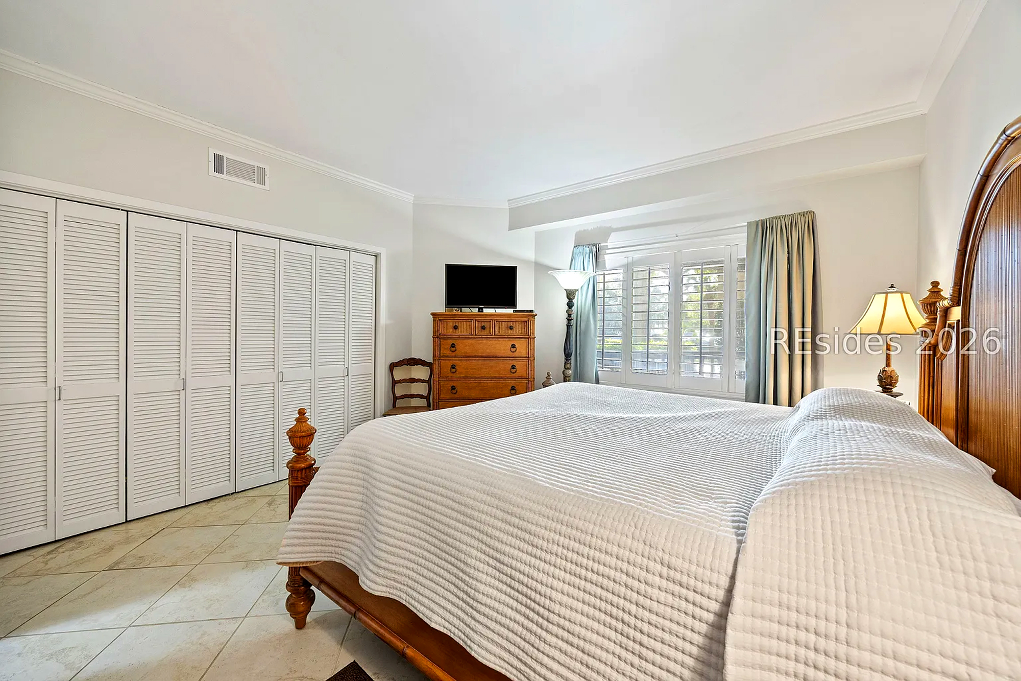 Carved wood bedframes and soft linens create an inviting sanctuary where morning rays filter through classic shutters. This airy bedroom pairs neutral tones with timeless furnishings for a truly peaceful stay.