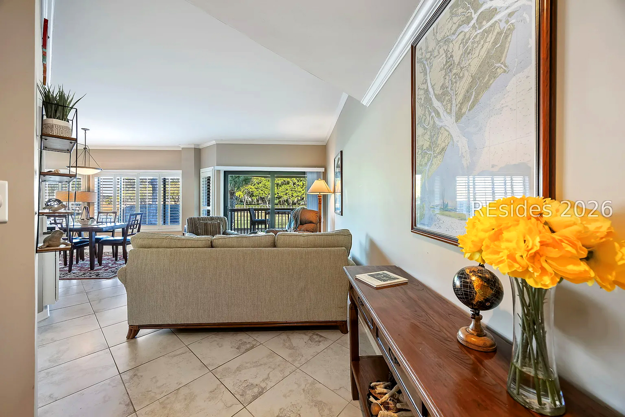 Sun-kissed interiors pair with a classic map and bright florals to create an air of nautical charm. Polished tiles and soft seating lead the eye toward garden views, offering a calm and airy space for quiet afternoons.