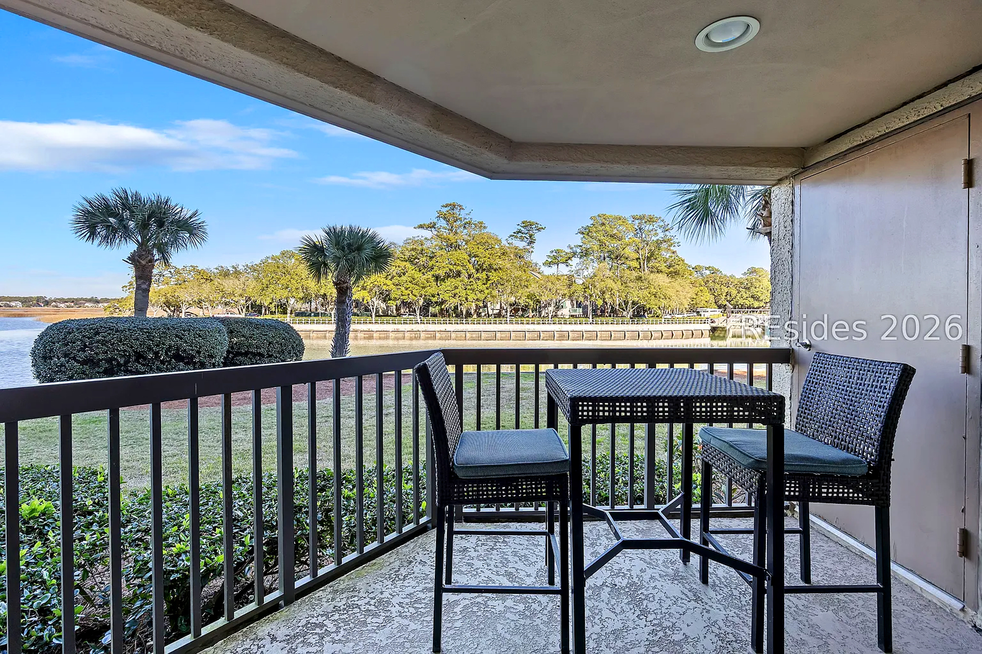 Wicker bistro seating invites you to linger over coffee while overlooking the calm water and swaying palms. This sheltered balcony offers a peaceful vantage point to watch the afternoon glow settle over the trees.