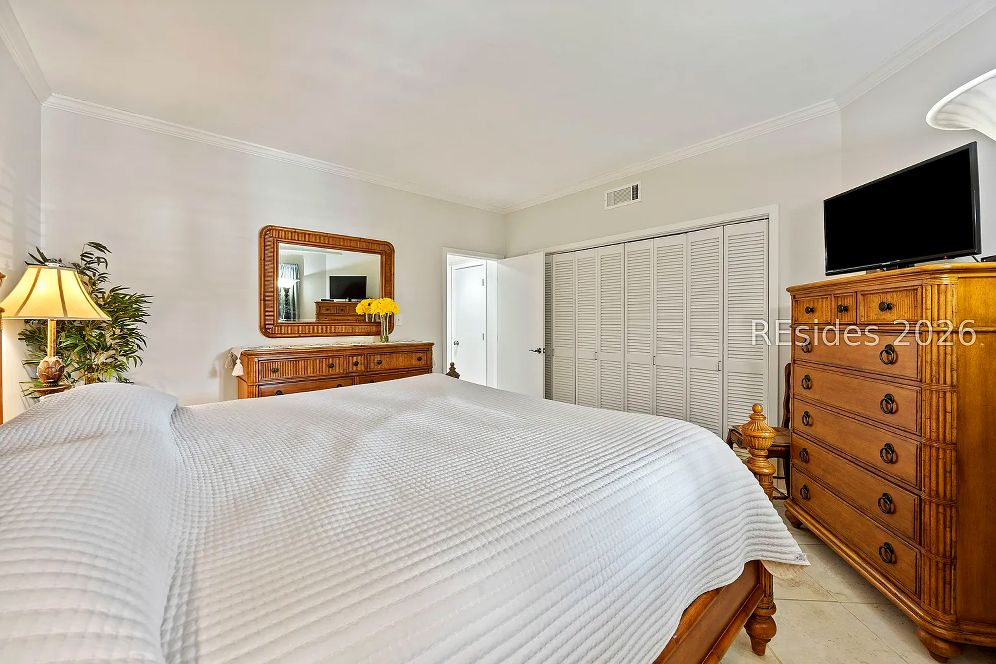 Natural wood dressers and a textured white quilt create an air of timeless comfort in this bright guest suite. Soft lamp illumination and fresh floral accents make the space feel incredibly calm and inviting for a restful night.