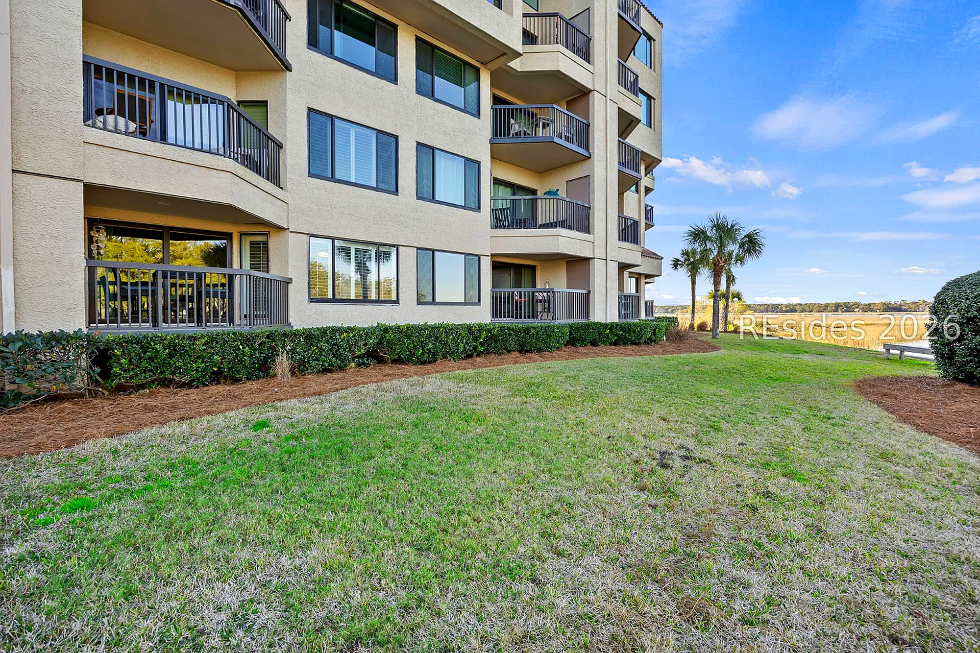 Textures highlight lawns meet the stucco facade of this quiet residence, where private balconies overlook a peaceful marsh landscape. Soft afternoon shadows dance across the grass, promising a tranquil stay by the water.