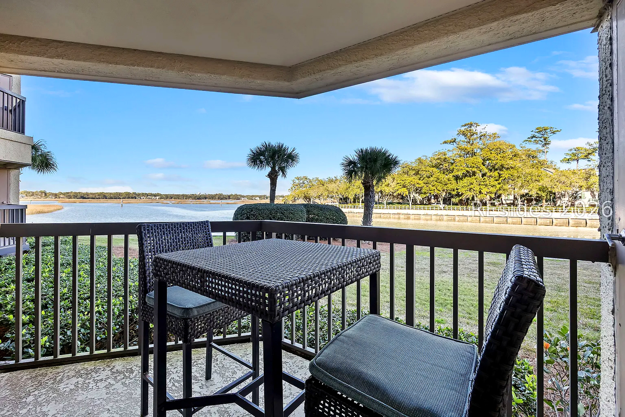 Sturdy resin bistro seating overlooks a calm waterway, offering a quiet perch for your morning coffee. Clean lines and fresh air define this shaded balcony, where the view stretches across manicured lawns to the distant palms.