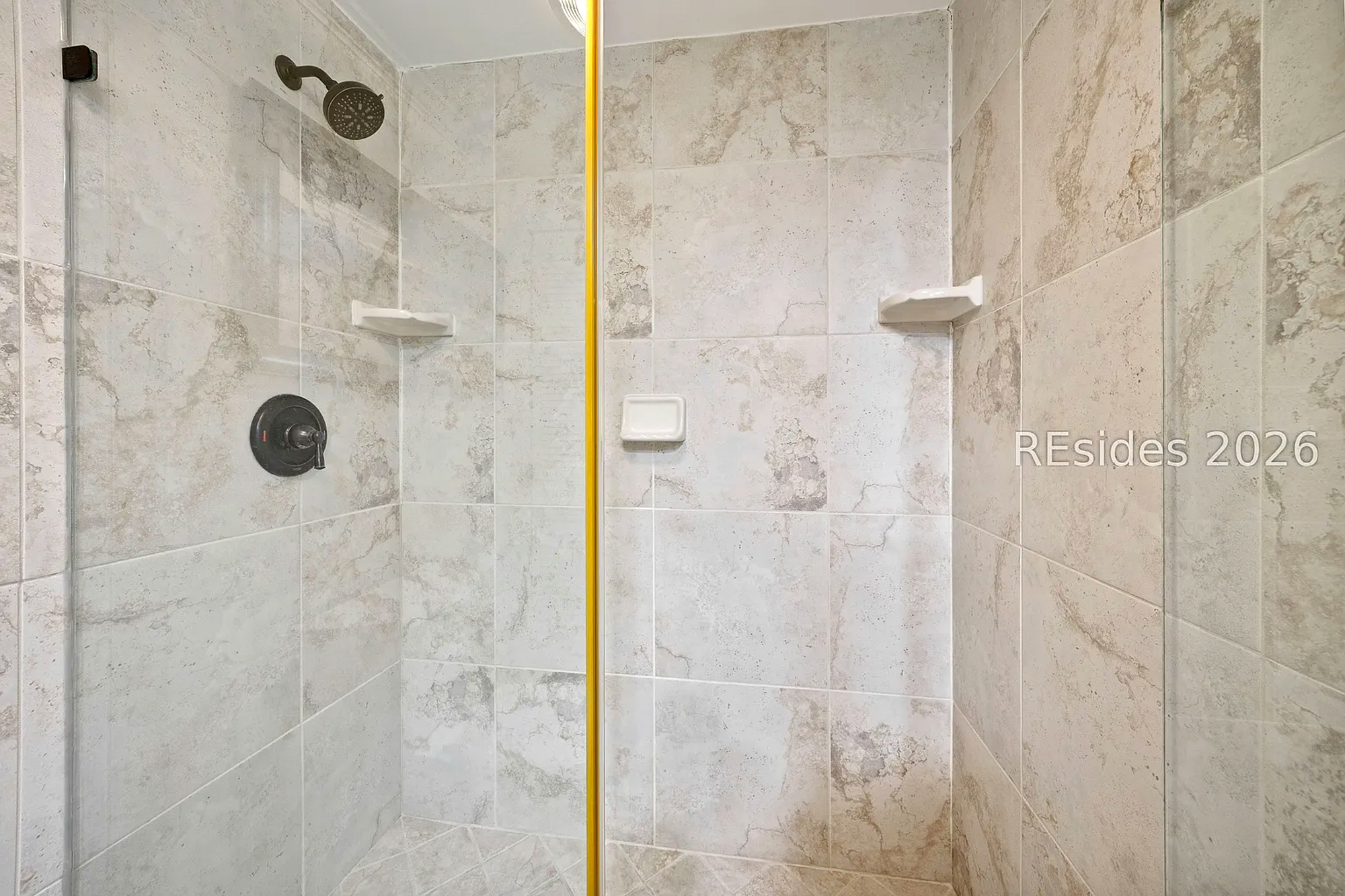 Sandstone hues and marbled tiles create a serene backdrop for a refreshing morning rinse. Matte bronze fixtures add a touch of modern elegance to this spacious walk-in shower.