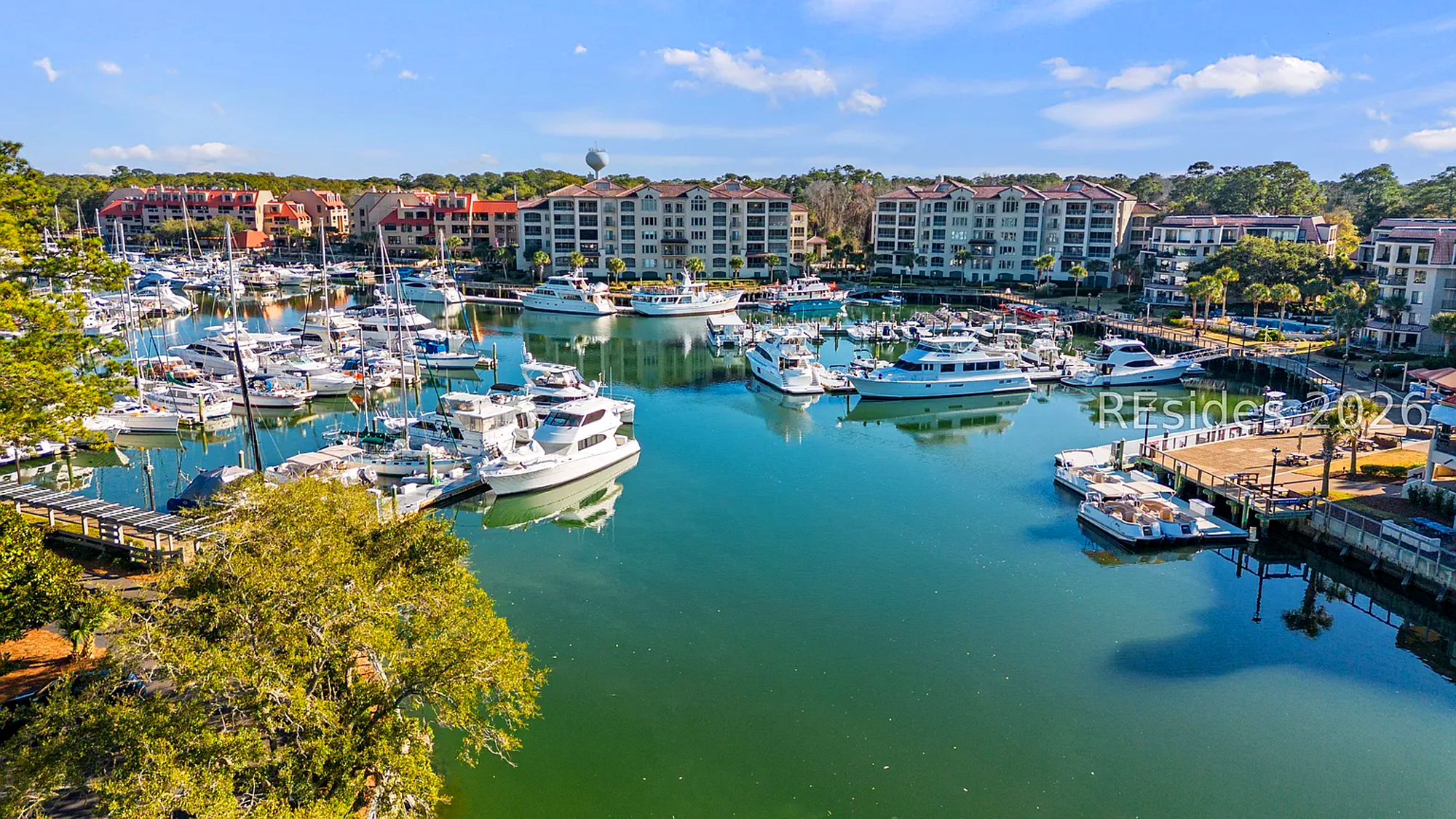 Sleek vessels rest on calm, teal waters under a vast sky, offering a picturesque view of maritime life. Mediterranean style buildings frame the cove, creating an inviting getaway for those who love the rhythm of the tides.