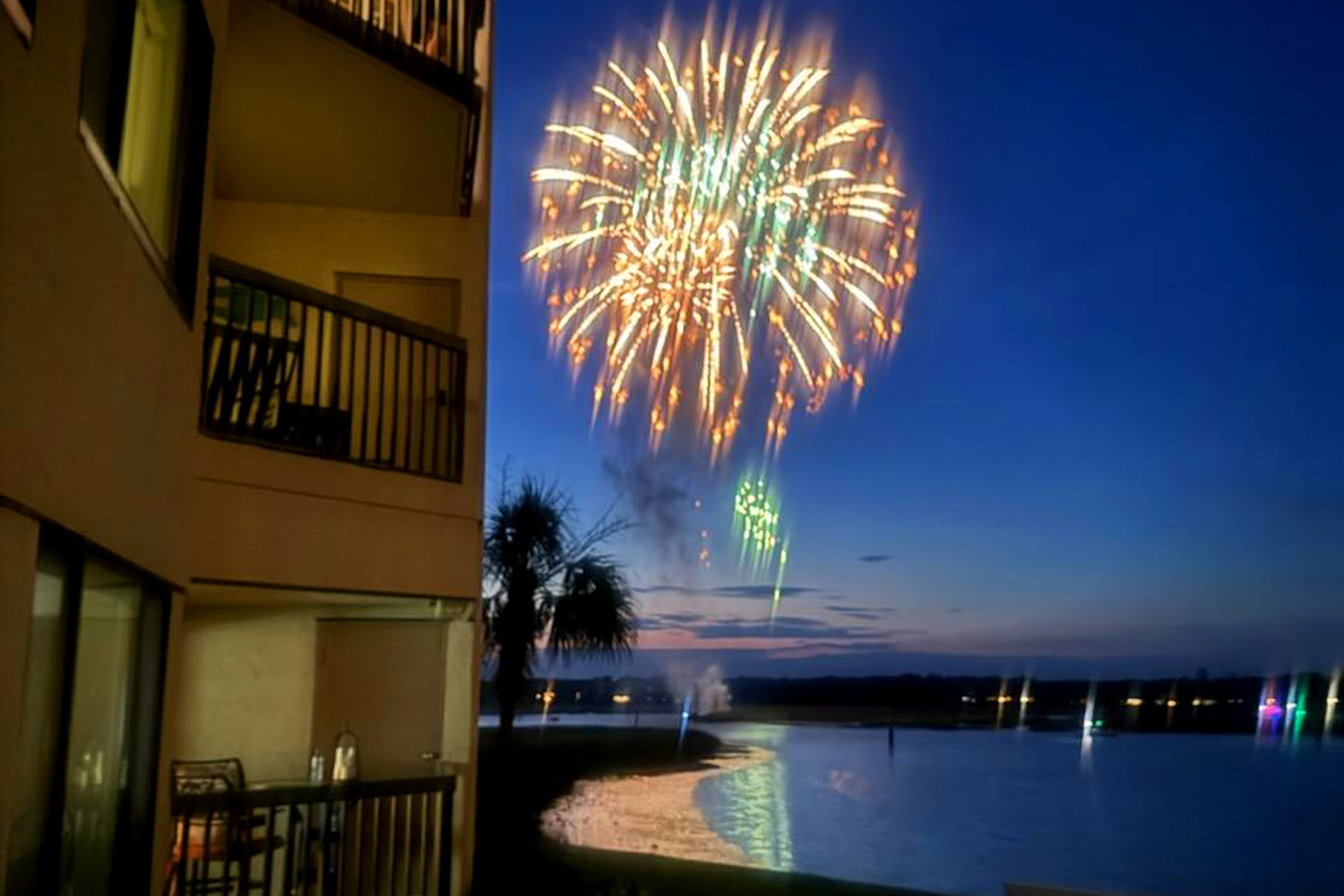 Fireworks erupt in a vivid display over the quiet lake, seen directly from the comfort of your private balcony. The night sky provides a dramatic backdrop for these shimmering colors reflecting off the gentle water.